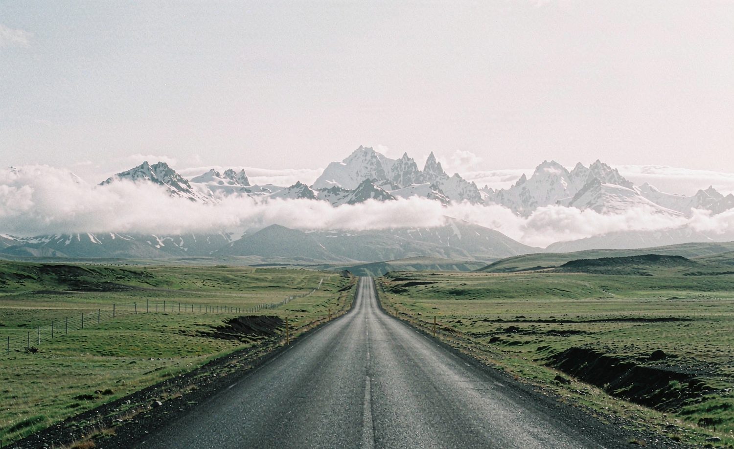 Route déserte traversant une prairie d’altitude, montagnes enneigées au fond